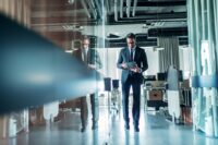 Ein Mann läuft einen Gang mit viel Glas entlang und macht sich Notizen zu Steuern beim Unternehmensverkauf